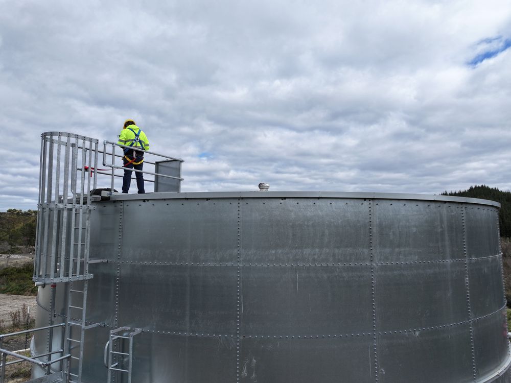 A worker in hi-vis on the railed platform at the top of a galvanised steel tank.