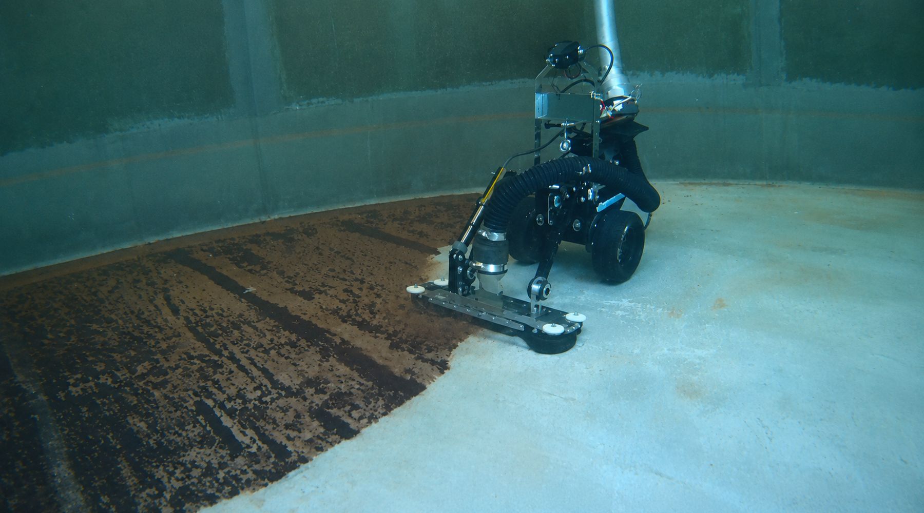 The VAC Boss crawler on a reservoir floor, with a clean strip of concrete beside the brown sediment it is removing.